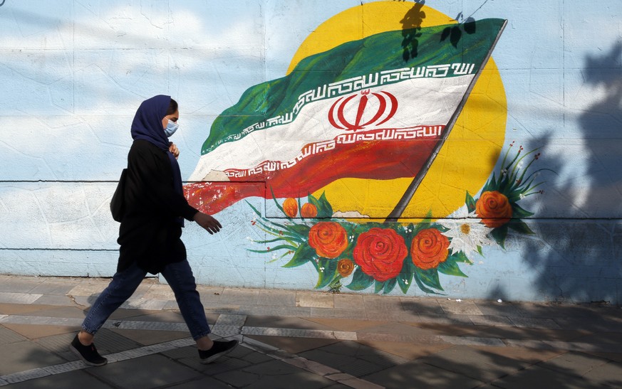 epa09143237 An Iranian woman wearing a face mask walks next to a wall painting of Iran&#039;s national flag on a street in Tehran, Iran, 18 April 2021. According to Iranian health ministry 405 people  ...