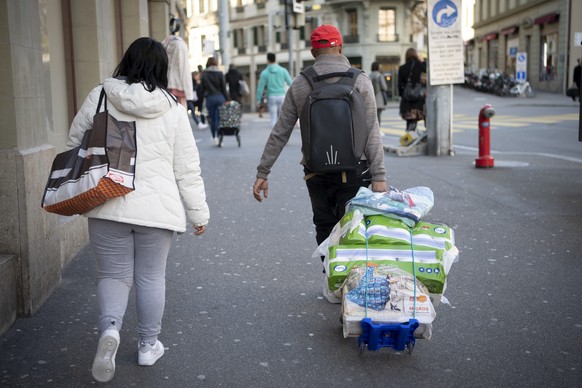 People walk down the street after making purchases, including toilet paper, during the Covid-19 Coronavirus pandemic, in Lausanne, Switzerland, Friday, March 13, 2020. (KEYSTONE/Jean-Christophe Bott)