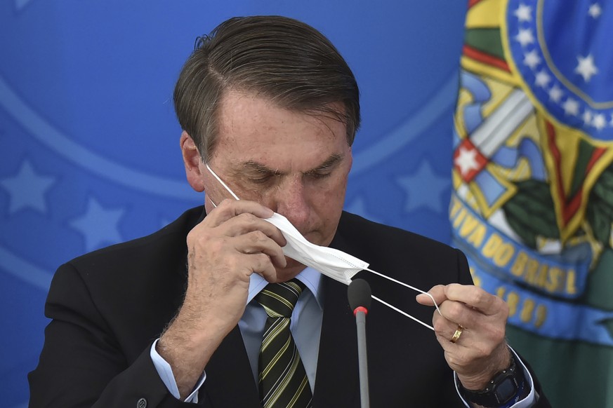 Brazil&#039;s President Jair Bolsonaro puts on a mask during a press conference on the new coronavirus at the Planalto Presidential Palace in Brasilia, Brazil, Wednesday, March 18, 2019. For most peop ...