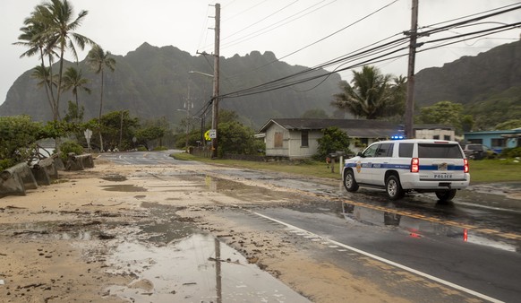 A police officer with the Honolulu Police Department inspects the sand and debris washed onto a closed portion of Kamehameha Highway, Sunday, July 26, 2020, in Kaaawa, Hawaii. High surf caused by Hurr ...