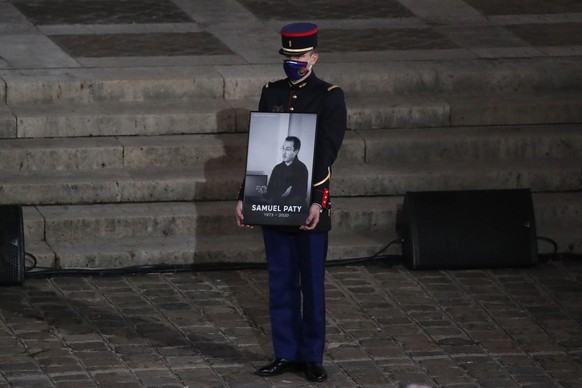 A Republican Guard holds a portrait of Samuel Paty in the courtyard of the Sorbonne university during a national memorial event, Wednesday, Oct. 21, 2020 in Paris. French history teacher Samuel Paty w ...