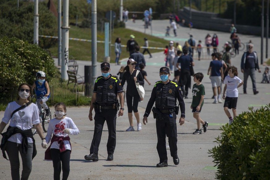 Catalan police officers patrol as families with their children walk along a boulevard in Barcelona, Spain, Sunday, April 26, 2020 as the lockdown to combat the spread of coronavirus continues. On Sund ...