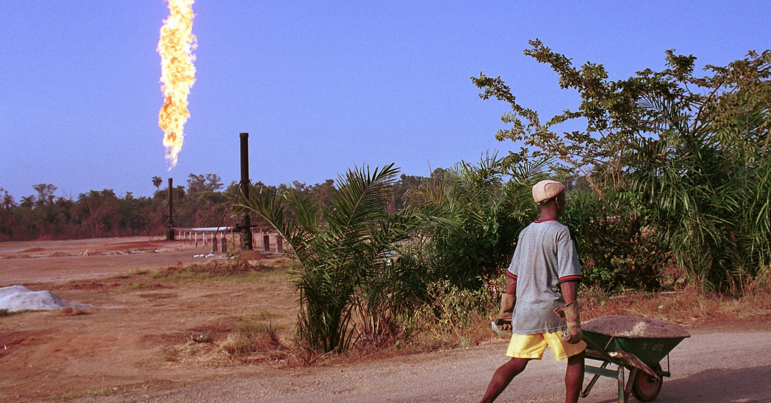390464 36: A villager walks past a column of fire from the Oshie flare station owned by Italian oil company Agip, March 8, 2001 near Akaraolu, Nigeria. The natural gas flare was lit in 1972 and has be ...