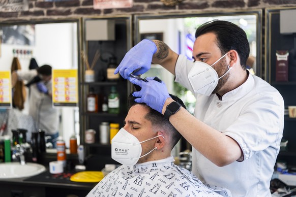 epa08386577 A hairdresser, wearing a protective face mask, cuts the hair of a client who also wears a protective face mask at the La Barberia shop during the spread of the pandemic Coronavirus (COVID- ...