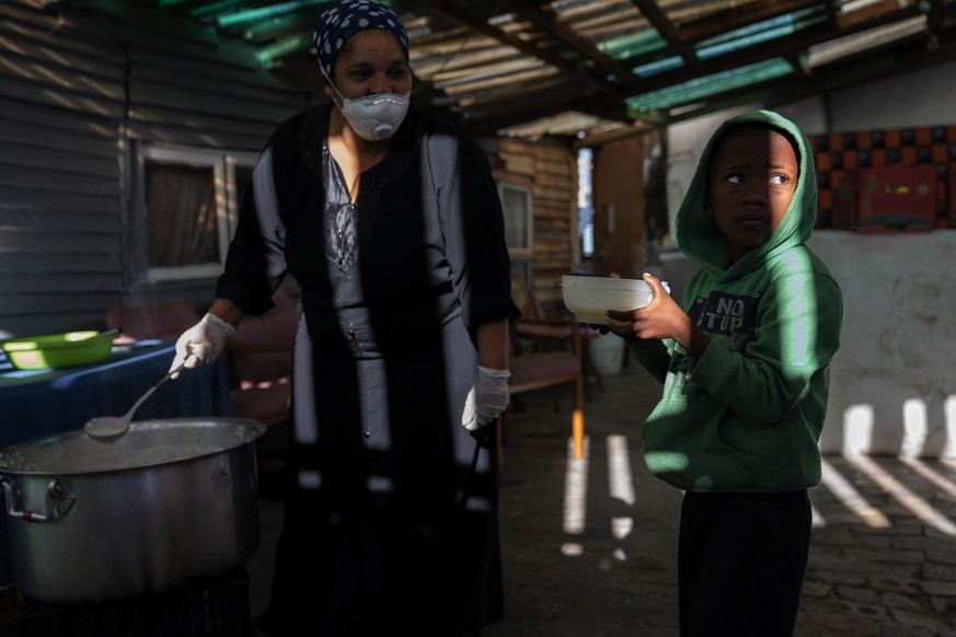 epaselect epa08372867 A South African child from the 7de Laan shack settlement receives a bowl of porridge from resident Kaltoma Samodien (L) who cooks for the 9 Miles Project Covid-19 community suppo ...