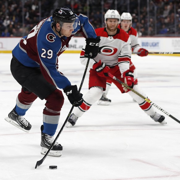 Colorado Avalanche center Nathan MacKinnon, front, shoots the puck as Carolina Hurricanes defenseman Jaccob Slavin covers in the first period of an NHL hockey game Monday, March 11, 2019, in Denver. ( ...