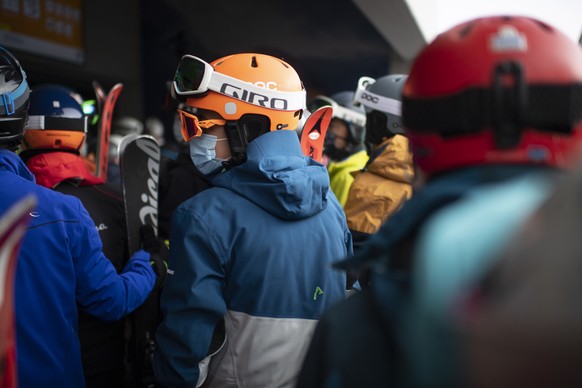 Menschen mit Schutzmasken warten auf die Parsenn-Bahn, aufgenommen zum Start der Skisaison, am Sonntag, 25. Oktober 2020, in Davos. Das Skigebiet Davos Klosters startet den Wochenendbetrieb. (KEYSTONE ...