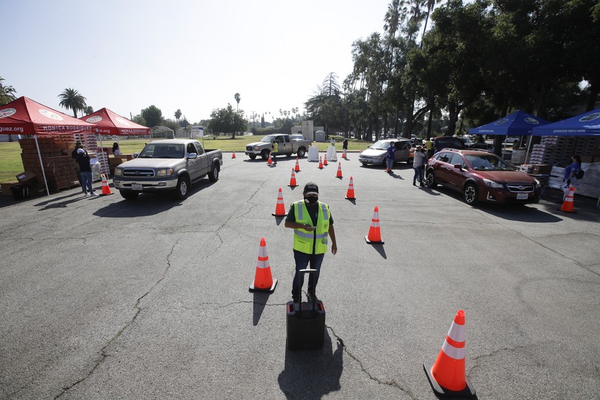 A volunteer stands in the middle of two vehicle lanes as cars line up at a food distribution center Wednesday, July 22, 2020, in the Mission Hills area of Los Angeles. (AP Photo/Marcio Jose Sanchez)