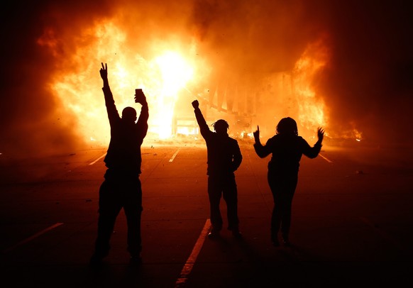 epa04502811 Protesters gesture in front of a burning auto parts store in Ferguson Missouri, USA, 25 November 2014. According to St Louis County Prosecuting Attorney, the Grand jury decided that Fergus ...