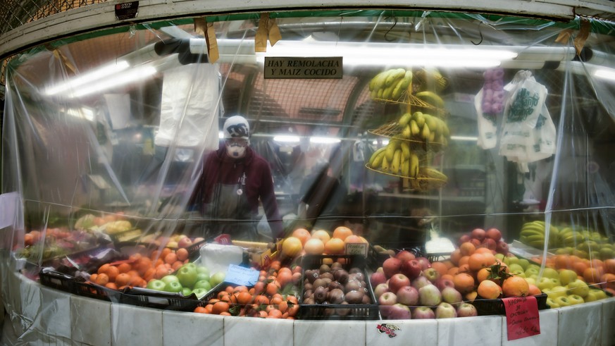 A worker wearing a face mask stands inside of a stall covered with a piece of plastic to prevent the spread of coronavirus, at a market in Pamplona, northern Spain, Thursday, April 2, 2020. The new co ...
