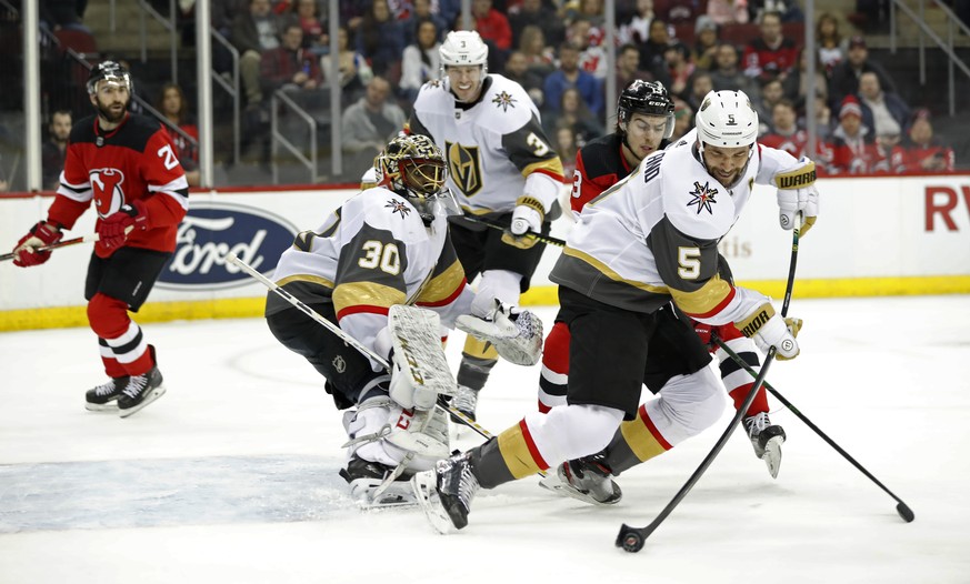 Vegas Golden Knights defenseman Deryk Engelland (5) tries to corral the puck away from New Jersey Devils center Nico Hischier (13) in front of Golden Knights goaltender Malcolm Subban (30) during the  ...