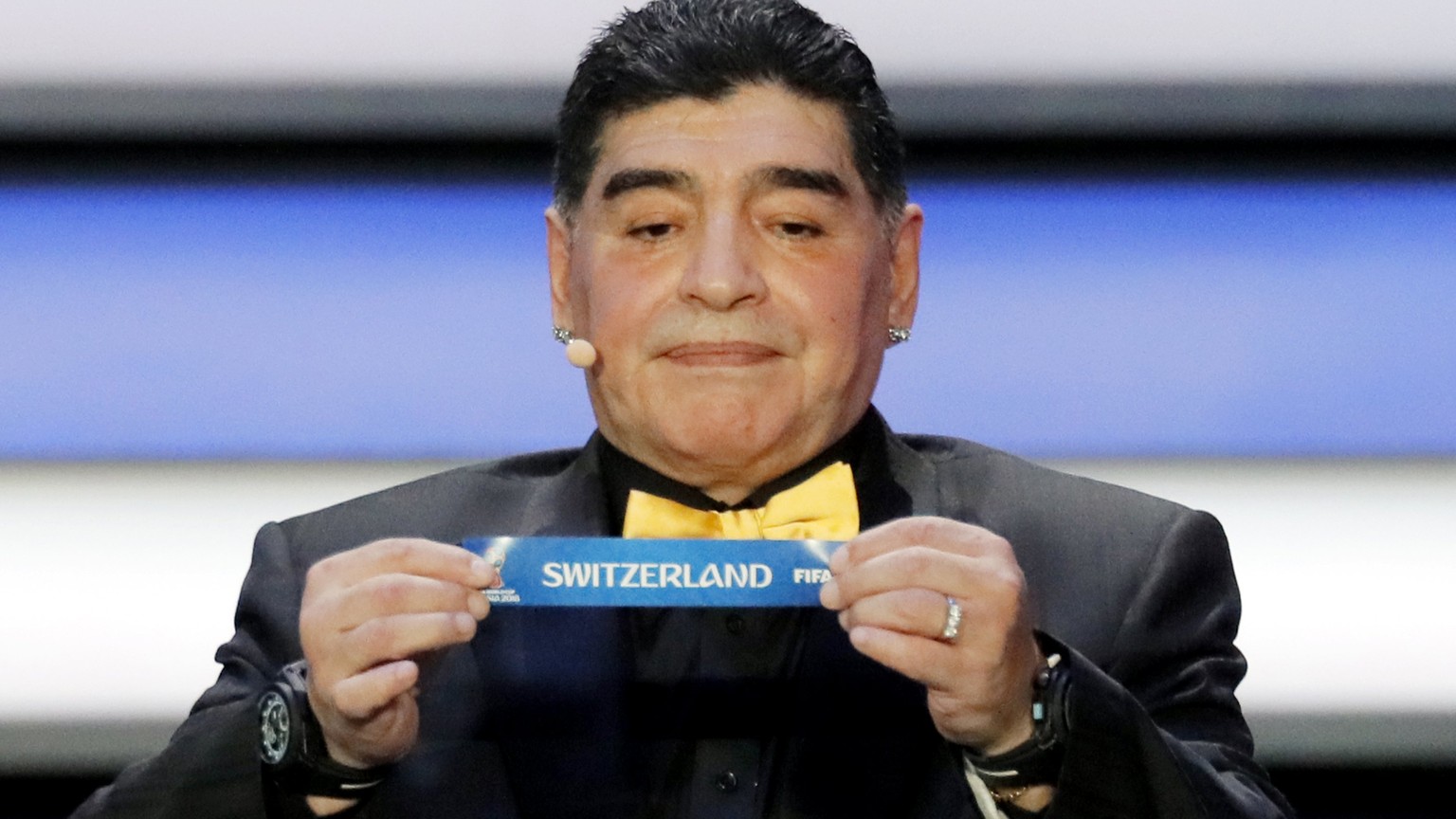 epa06361881 Draw assistant, former Argentine international Diego Maradona shows the ticket of Switzerland during the Final Draw of the FIFA World Cup 2018 at the State Kremlin Palace in Moscow, Russia ...
