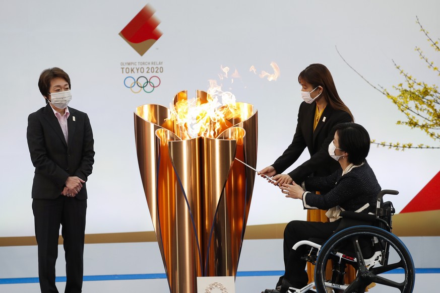 Tokyo 2020 President Seiko Hashimoto, left, watches Japanese actress Satomi Ishihara and Paralympian Aki Taguchi light the celebration cauldron on the first day of the Tokyo 2020 Olympic torch relay i ...