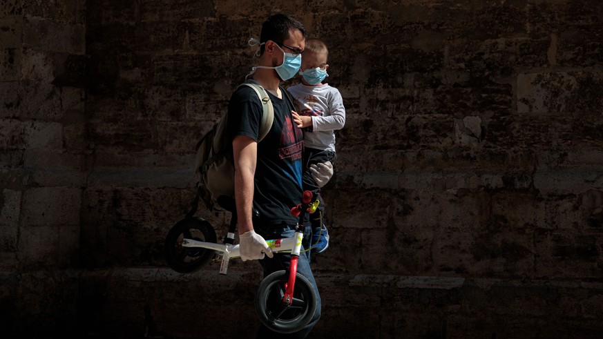 epa08385430 A man walks with his son on his arms amid the ongoing coronavirus COVID-19 pandemic in Valencia, Spain, 26 April 2020, on the first day that minors have been allowed for an hour a day outs ...