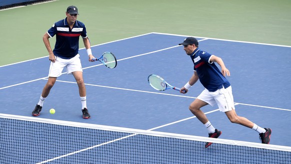 Mike Bryan, left, returns a shot as his brother Bob Bryan, looks on during a first round doubles match against Hubert Hurkacz, of Poland, and Vasek Pospisil, of Canada, at the US Open tennis champions ...