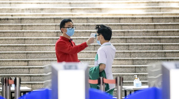 epa08386872 A teacher (L) measures the temperature of a pupil at the entrance of the Nanwu school in Guangzhou, Guangdong province, China, 27 April 2020, amid the ongoing coronavirus COVID-19 pandemic ...