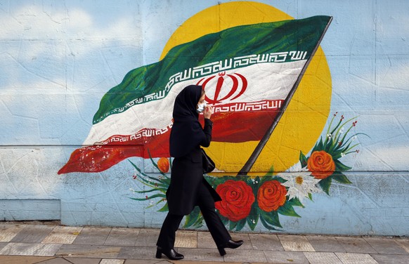 epa08820545 An Iranian woman wearing a face mask walk past next to a wall painting of Iran?s national flag in a street in Tehran, Iran, 14 November 2020. According to the Iranian Health ministry, Iran ...