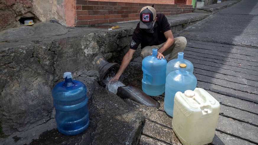 epa08308218 A man collects water from a broken pipe in Caracas, Venezuela, 19 March 2020. A Venezuelan Parliament commission reported that 80 percent of households in Venezuela occasionally receive wa ...
