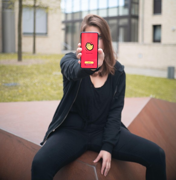 Auflösung zum Teaserbild: Eine junge Frau hält ein Smartphone mit der Houseparty-App, die es ermöglicht, in Gruppen virtuelle Videopartys zu feiern.