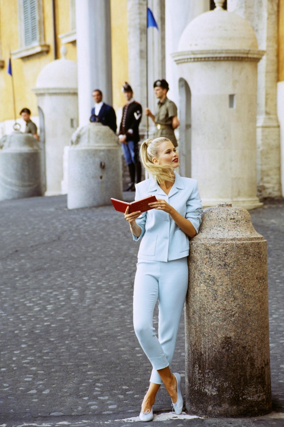 ITALY - DECEMBER 1: Model Claudia Schiffer, with book on Roman street, wearing capri pants and spencer-style jacket in aqua blue, by Mark Eisen CREDIT MUST READ: Arthur Elgort/Conde Nast via Getty Ima ...