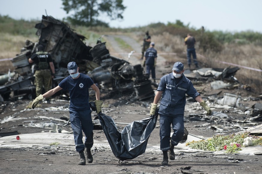 FOR STORY UKRAINE MH17 WHERE THINGS STAND - FILE - In this Sunday, July 20, 2014 file photo Ukrainian Emergency workers carry a victim&#039;s body in a body bag as pro-Russian fighters stand guard at  ...