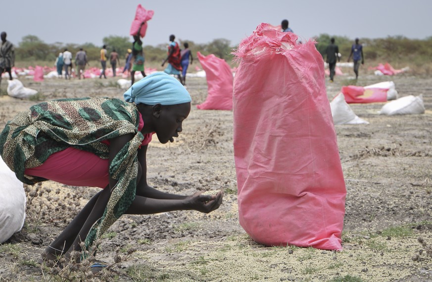 FILE - In this Wednesday, May 2, 2018 file photo, a woman scoops fallen sorghum grain off the ground after an aerial food drop by the World Food Program (WFP) in the town of Kandak, South Sudan. South ...