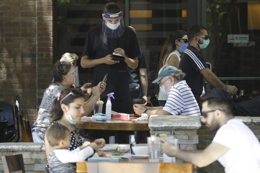 A waiter takes a food order Saturday, July 18, 2020, in Burbank, Calif. The city of Burbank has closed off some streets in the downtown district to allow restaurants to expand their outdoor seating ar ...
