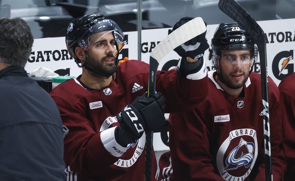 Colorado Avalanche defenseman Mark Barberio, left, cleans off the blade of his stick as defenseman Conor Timmins looks on in the team box during an NHL hockey practice Monday, July 20, 2020, in Denver ...