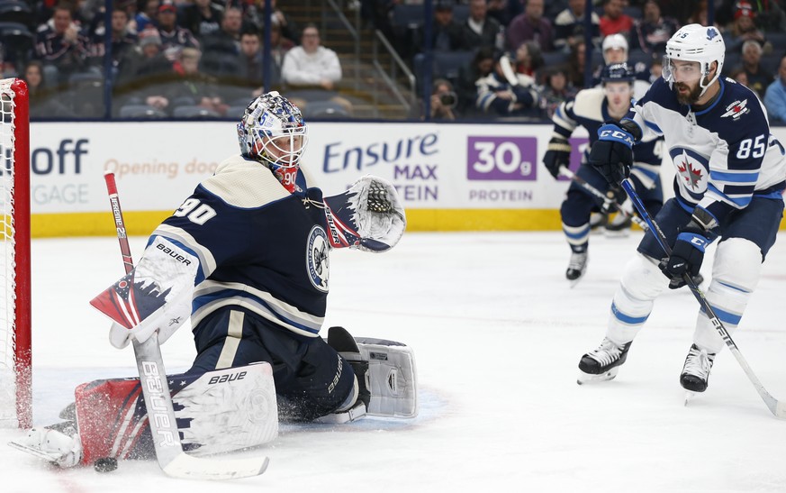 Columbus Blue Jackets&#039; Elvis Merzlikins, left, of Latvia, makes a save against Winnipeg Jets&#039; Mathieu Perreault during the third period of an NHL hockey game Wednesday, Jan. 22, 2020, in Col ...
