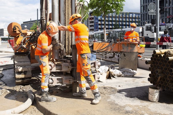 epa08387349 Workers wearing protective face masks, as recommended by Swiss authorities as a precaution against the spread of the coronavirus COVID-19, remove drilling tubes at a construction site in G ...