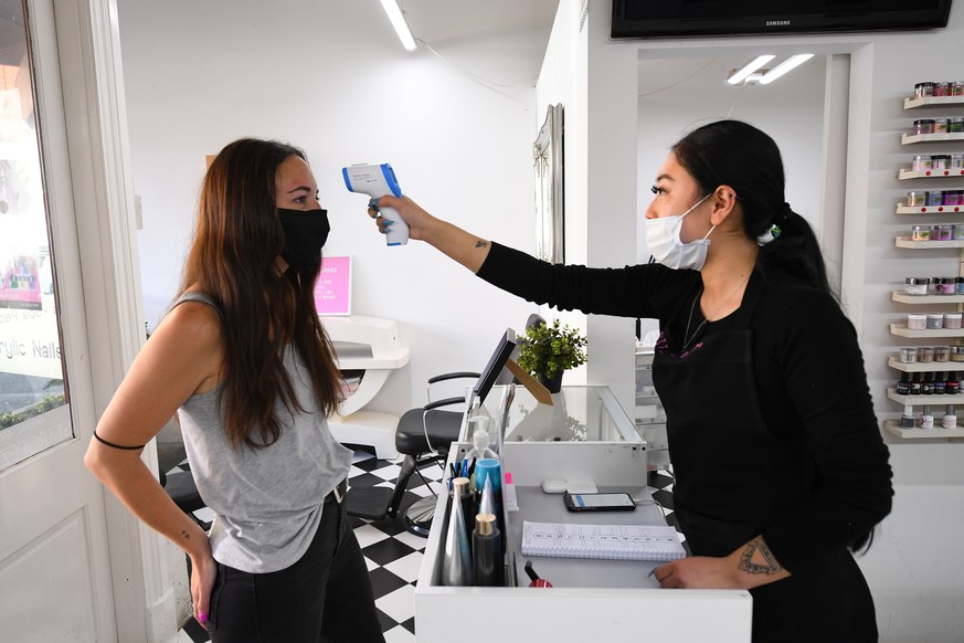 epa08779674 A beautician (R) takes the temperature of a client at a nail salon in Collingwood, Melbourne, Australia, 28 October 2020. Further coronavirus restrictions were eased in metropolitan Melbou ...