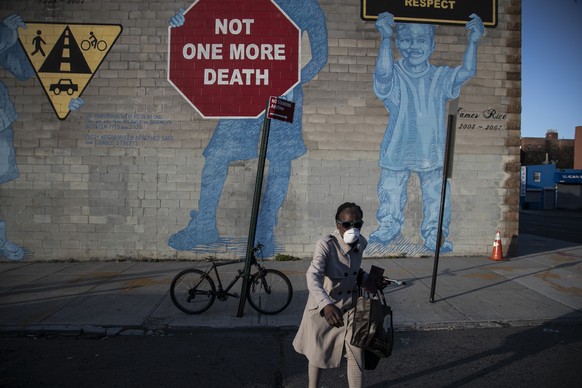 A woman wearing a mask crosses the street in front of a mural about traffic accidents reading, &quot;NOT ONE MORE DEATH&quot; in the Brooklyn borough of New York Friday, March 27, 2020. The new corona ...