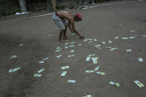 An man plays around with discarded 50 Bolivar bills during a break in a pick football game, outside a building occupied by squatting families in Caracas, Venezuela, Tuesday, May 7, 2019. Due to hyperi ...