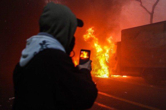 epaselect epa08864958 A man records on his phone a car burning during a protest against France&#039;s controversial global security law, during a protest in a street between Porte des Lilas and Gambet ...