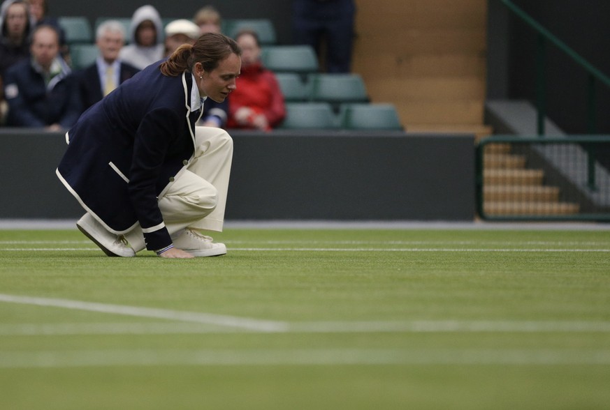 An official feels the grass as Agnieszka Radwanska of Poland and Maria Kirilenko of Russia play a quarterfinals match at the All England Lawn Tennis Championships at Wimbledon, England, Tuesday, July  ...