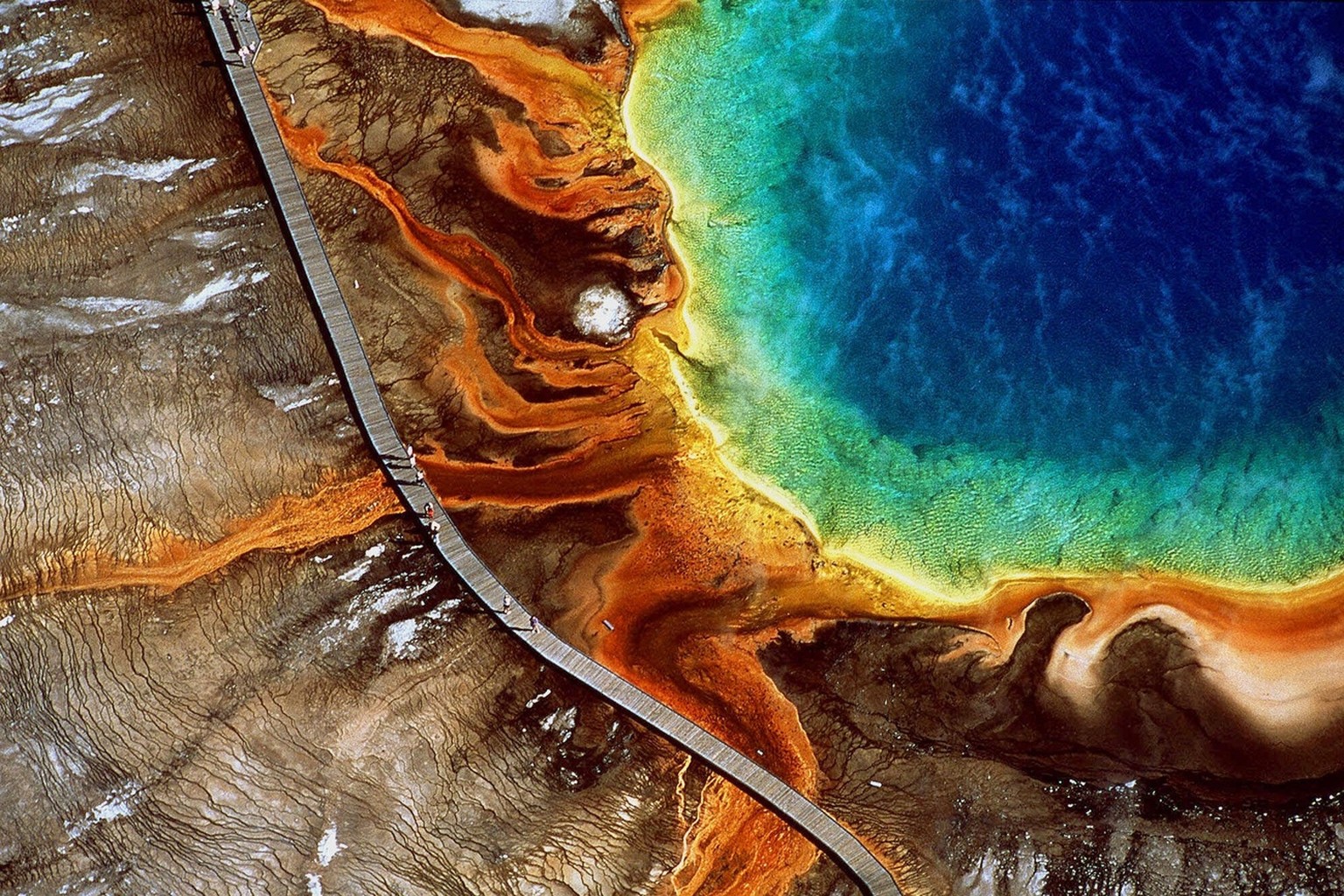 Tourists walk along the boardwalk at the edge of the Grand Prismatic Spring in Yellowstone National Park, Wyoming, in this aerial photo, date unknown. The image is part of a new photo exhibit and coff ...
