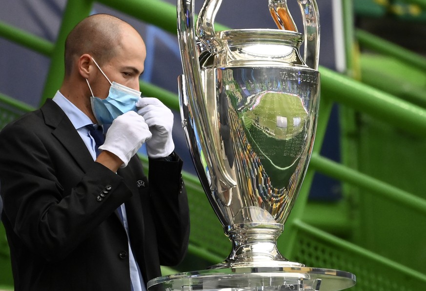 A staff member sets the mask by the Champions League trophy before the Champions League semifinal soccer match between Lyon and Bayern at the Jose Alvalade stadium in Lisbon, Portugal, Wednesday, Aug. ...