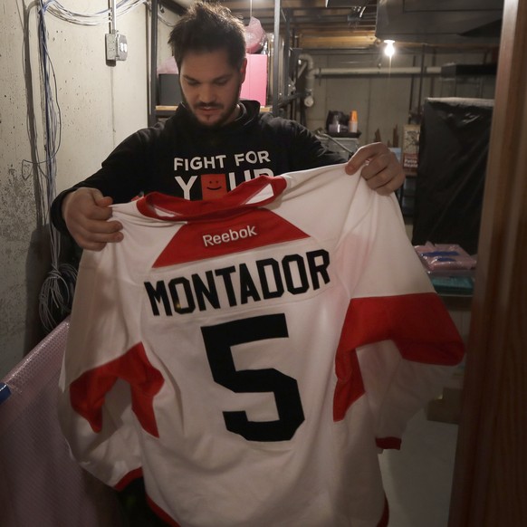 In this Tuesday, April 2, 2019, photo, former NHL player Dan Carcillo looks at the hockey sweater of his friend Steve Montador in the basement of his rural home in Homer Glen, Ill. Montador is one of  ...
