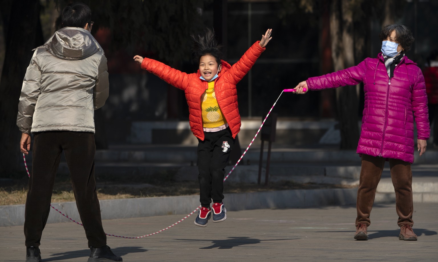 A woman wearing a face mask to protect against the spread of the coronavirus twirls a jumprope for a girl at Ditan Park in Beijing, Tuesday, Feb. 9, 2021. The park, which would normally host one of th ...