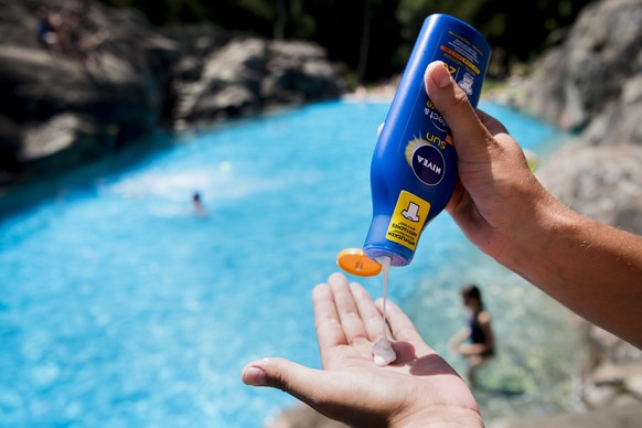 epa07672614 A person puts on sunscreen in front of the Marecottes swimming pool on a hot summer day in the village of Les Marecottes in Valais, Switzerland, 25 June 2019. Switzerland is preparing to f ...