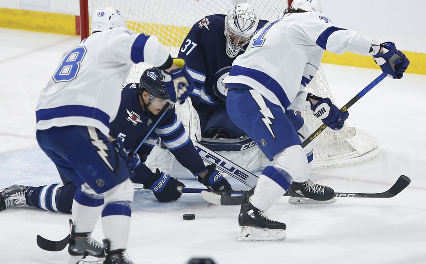 Winnipeg Jets goaltender Connor Hellebuyck (37) watches the puck Tampa Bay Lightning&#039;s Ondrej Palat (18) and Anthony Cirelli (71) look for the rebound and Jets&#039; Luca Sbisa (5) defends during ...