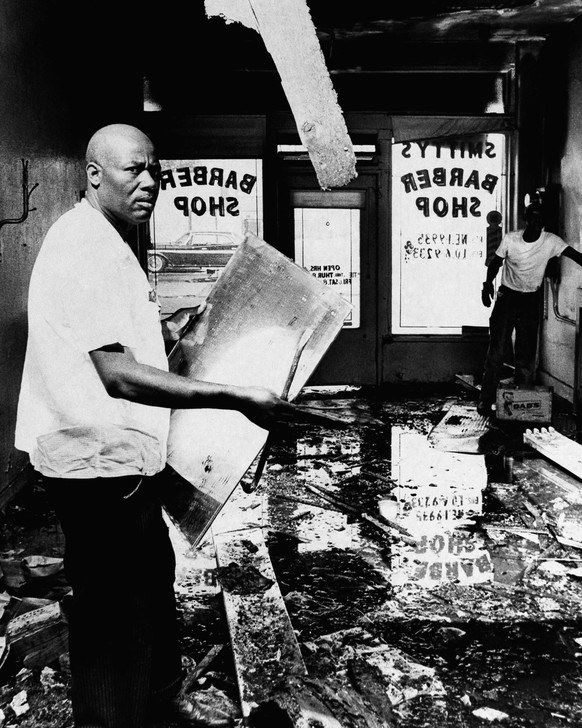 FILE - In this Aug. 17, 1965 file photo, A.Z. Smith, a victim of the Los Angeles riots, checks the damage to his barber shop in the Watts area of Los Angeles. Business establishments owned by whites w ...