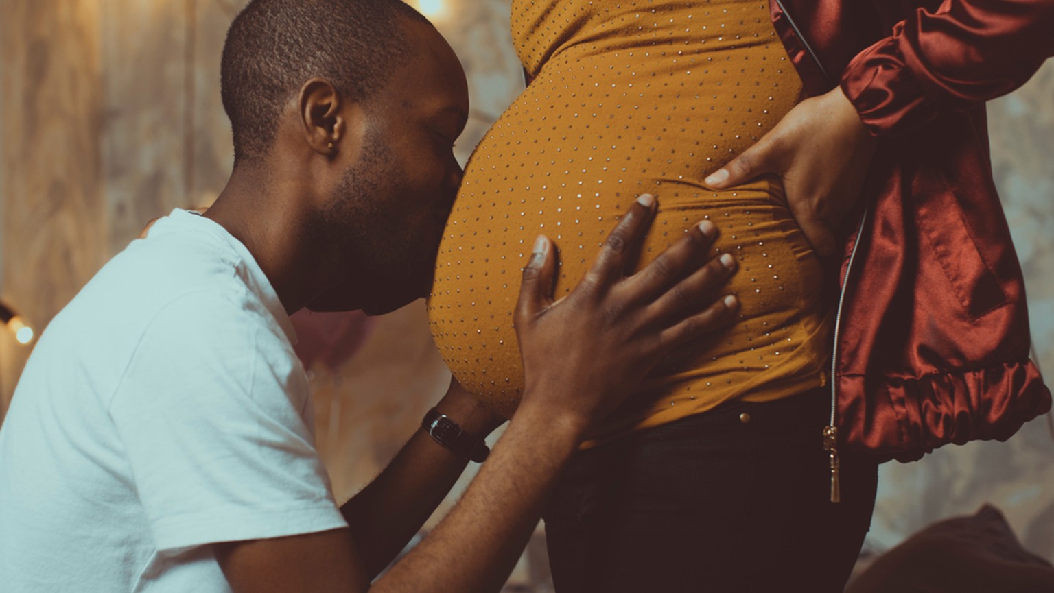 Mann küsst Bauch einer schwangeren Frau.