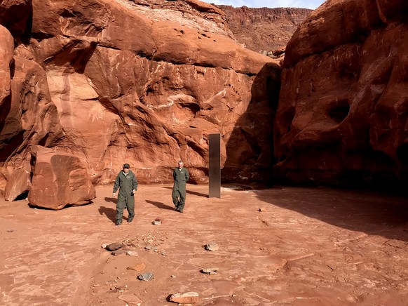 This Nov. 18, 2020 photo provided by the Utah Department of Public Safety shows Utah state workers walking near a metal monolith in the ground in a remote area of red rock in Utah. The smooth, tall st ...