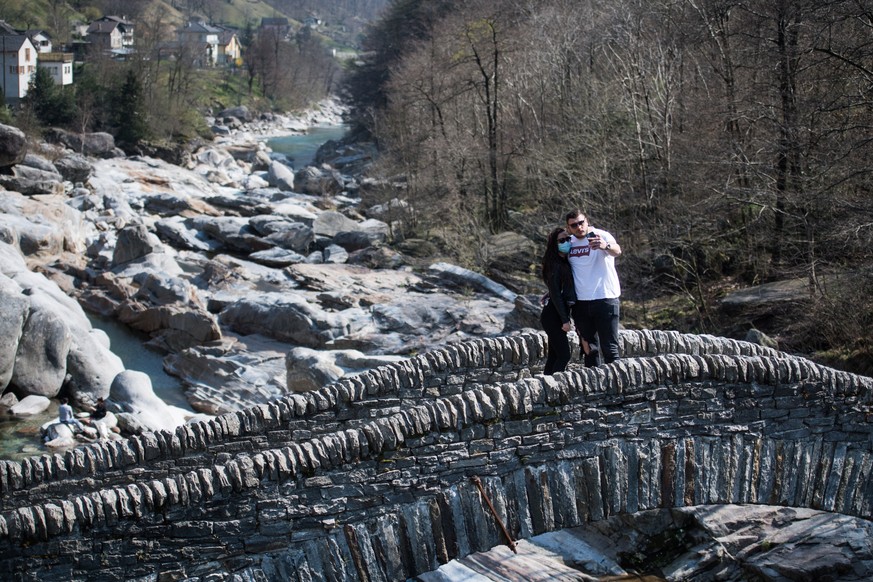 epa08344440 A couple takes a selfie on the famous Roman bridge in the Verzasca Valley, in Lavertezzo, Switzerland, 05 April 2020. Normally, the Verzasca Valley is visited on weekends by tourists from  ...