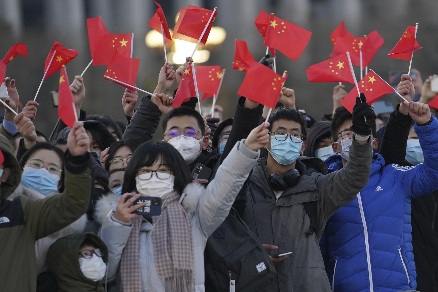 In this photo released by Xinhua News Agency, visitors to Tiananmen Square wave Chinese national flags as they attend the flag raising ceremony on Tiananmen Square in Beijing Friday, Jan. 1, 2021. (Ju ...