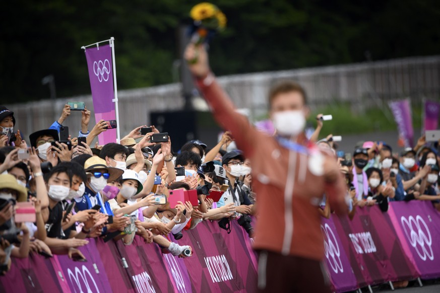 epa09366772 Japanese spectators looking at Silver medal winner Mathias Flueckiger of Switzerland reacting with his medal during the victory ceremony after the men&#039;s Cross-country Mountain Bike, M ...