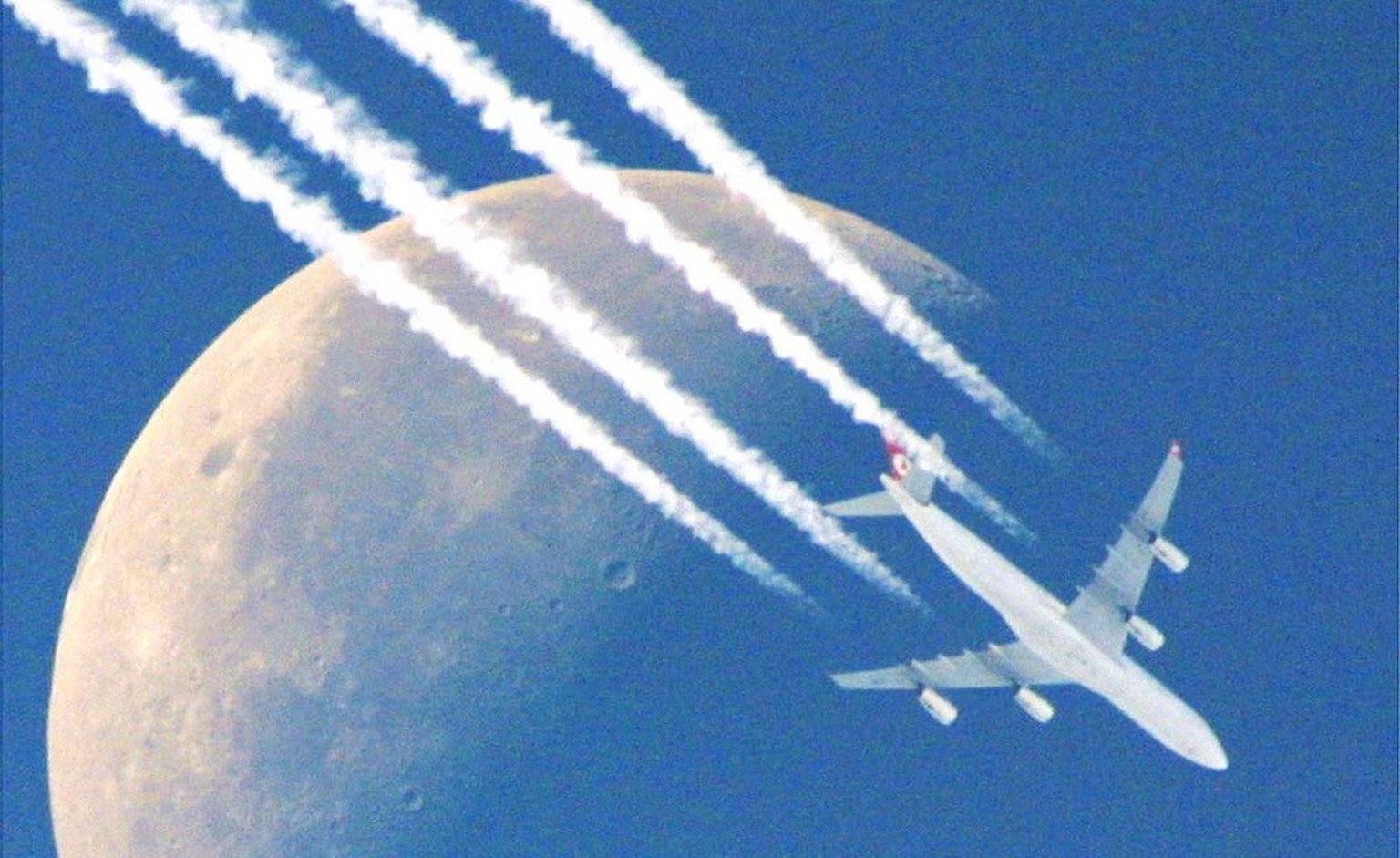 A north-west bound four-engine plane flies past the half moon, leaving its contrails in the clear skies over Frankfurt, Germany, Monday morning, Sept. 30, 2002, as clear early autumn weather prevails  ...
