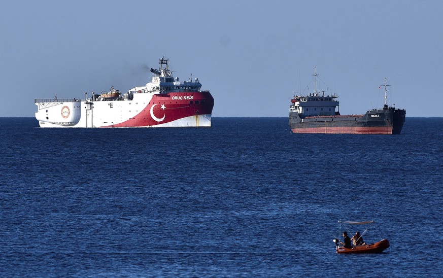 In this photograph taken from the Mediterranean shores near the city of Antalya, Turkey, a merchant ship, top right, sails past the research vessel Oruc Reis, Thursday, July 23, 2020. Greece has warne ...