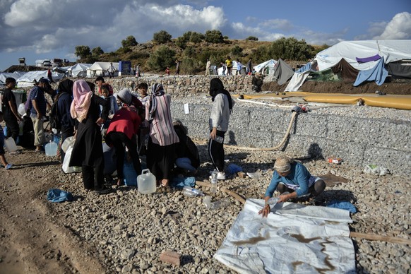Migrants collect water as others clean their belongings after a rainstorm at the Kara Tepe refugee camp, on the northeastern Aegean island of Lesbos, Greece, Wednesday, Oct. 14, 2020. Around 7,600 ref ...